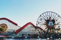 Vibrant image of a roller coaster and Mickey Mouse Ferris wheel at a theme park. Park hopping.