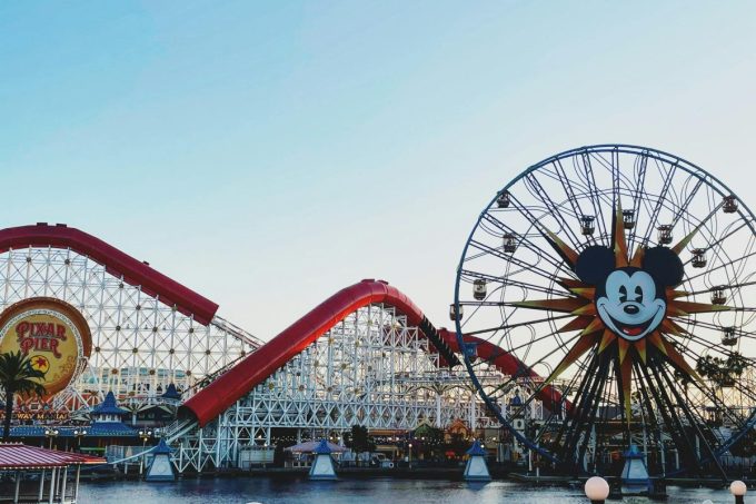 Vibrant image of a roller coaster and Mickey Mouse Ferris wheel at a theme park. Park hopping.